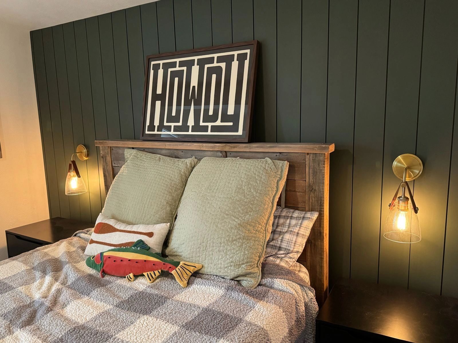Bedroom with hardwired wall sconces on either side of the bed against dark panelling.